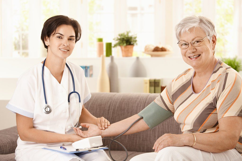 Stock photo of a caregiver checking a senior's blood pressure in a warm room. Models are not affiliated with this center.